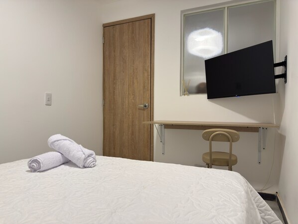 Ein Schlafzimmer mit einem Bett, einer Holztür, einem angebrachten Fernseher und einem kleinen Stuhl.