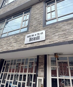Eine Gebäudefassade mit steiniger Textur, mehreren Fenstern und einem Schild mit der Aufschrift 'Calle 66 # 76-43 Brasil'.