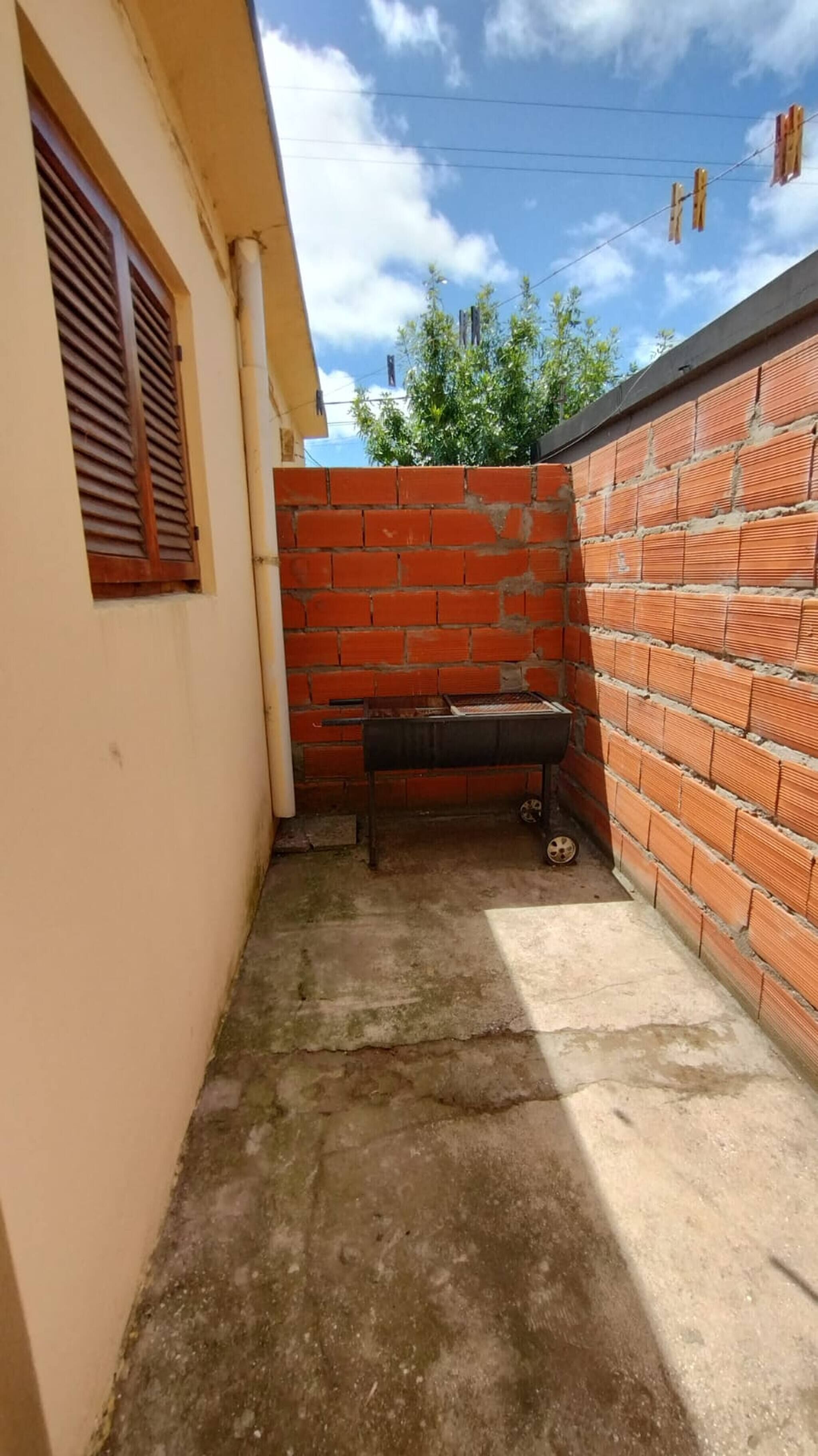 Un petit espace extérieur avec un mur en briques, un sol en béton et un gril en métal.