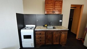 A compact kitchen with a gas stove, oven, wooden cabinets, and a marble countertop. - Studio Apartment, Special Winter (Santa Teresita)