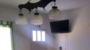 A compact room with a dining table, chairs, a TV mounted on the wall, a small cabinet, and a door with windows. - Studio Apartment, Special Winter (Santa Teresita)