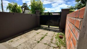 A paved courtyard with a black gate, a brick wall, and a potted plant. - Studio Apartment, Special Winter (Santa Teresita)