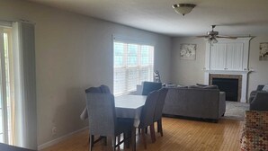 Un salon spacieux comprenant un coin repas, une cheminée et un ventilateur de plafond.