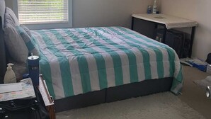 Une chambre à coucher comprenant un lit, un bureau, un ventilateur de plafond, une fenêtre avec des stores et un tapis.