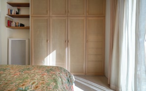 Ein Schlafzimmer mit Bett, Schrank, Heizkörper und Bücherregal.