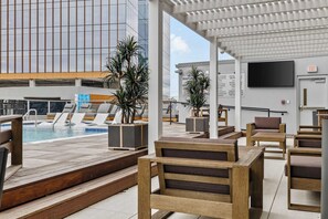 Ein Poolbereich auf dem Dach mit Holzmöbeln, einem Pool und Blick auf ein modernes Gebäude.