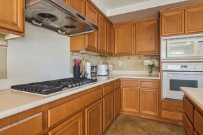 Una cocina con armarios de madera, estufa a gas, microondas y refrigerador.