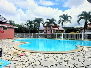 Ein Pool mit einer Steindeck, umgeben von einem weißen Zaun, Palmen und einem Gebäude mit rotem Dach.