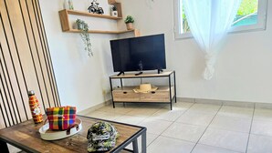 Una sala de estar con una mesa de centro de madera, un televisor sobre un mueble bajo y un ventanal con cortinas.