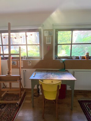 A room with a table, chair, radiator, and windows with views of greenery.