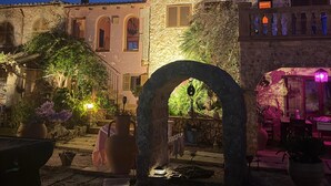 Un bâtiment en pierre doté d’une arche, de plantes en pot et d’un espace extérieur aménagé pour s’asseoir.
