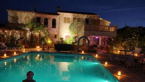Une piscine illuminée par des bougies la nuit, une statue et un bâtiment en arrière-plan.