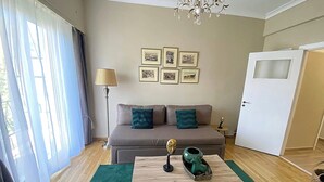 Olohuoneessa on sohva, sohvapöytä, lamppu ja seinällä on kehystettyjä valokuvia tai tauluja.