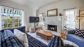 Ein Wohnzimmer mit Kamin, Fernseher und Blick auf einen Garten durch große Fenster.