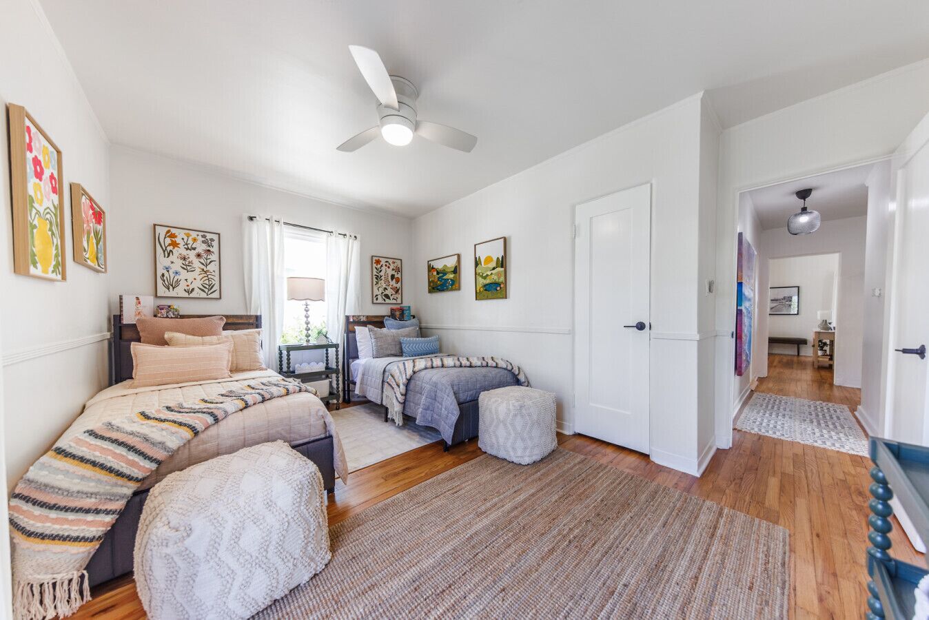 A bedroom with two beds, a ceiling fan, and a door leading to another room.