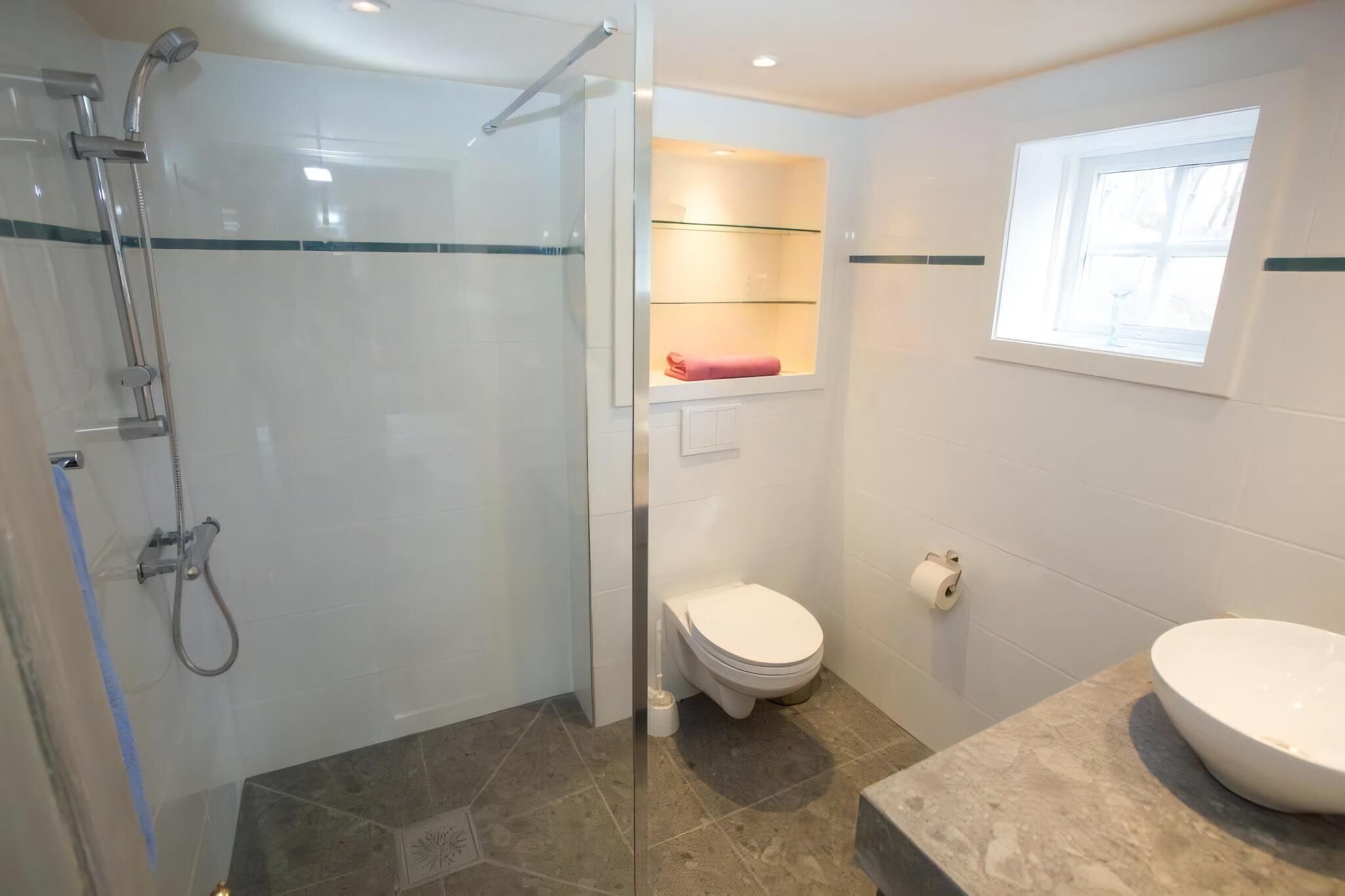 A bathroom with a glass-enclosed shower, a toilet, a sink, and a window.