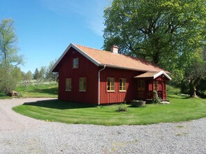 Ein rotes Holzhaus mit geneigtem Dach, einer Schotterauffahrt und einem gepflegten Rasen.