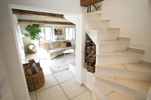 Eine Treppe mit Holzbalkon, ein Wohnzimmer mit Sofa und Couchtisch sowie ein großes Fenster.
