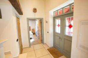 Un couloir avec une porte en bois, un paillasson et un sol carrelé.