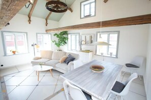 Ein geräumiges Wohnzimmer mit einem weißen Sofa, einem Esstisch und einem großen Fenster.