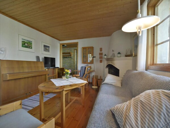 A cozy room with a wooden ceiling, a sofa, a TV, a dining table with a vase, and a fireplace.
