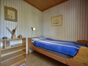 A room with a bunk bed, striped wallpaper, a shelf with decorative items, and framed pictures on the wall.