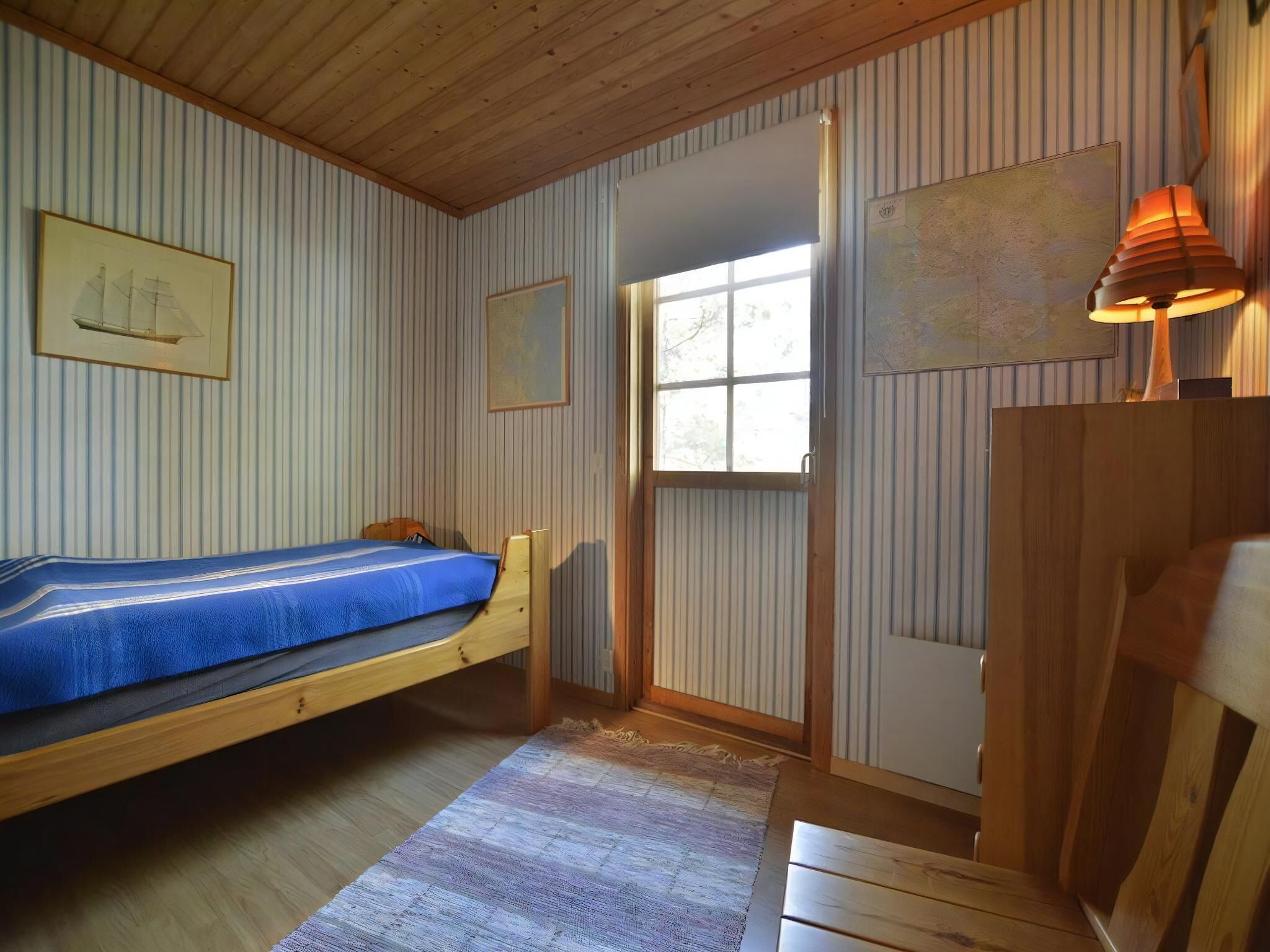 A single bed with a blue bedspread in a room with wooden walls and a window.