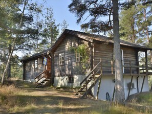 A rustic cabin with a wooden exterior, a staircase leading to the entrance, and a flag on the left side. - Lovely log house with a view of the sea (Figeholm)