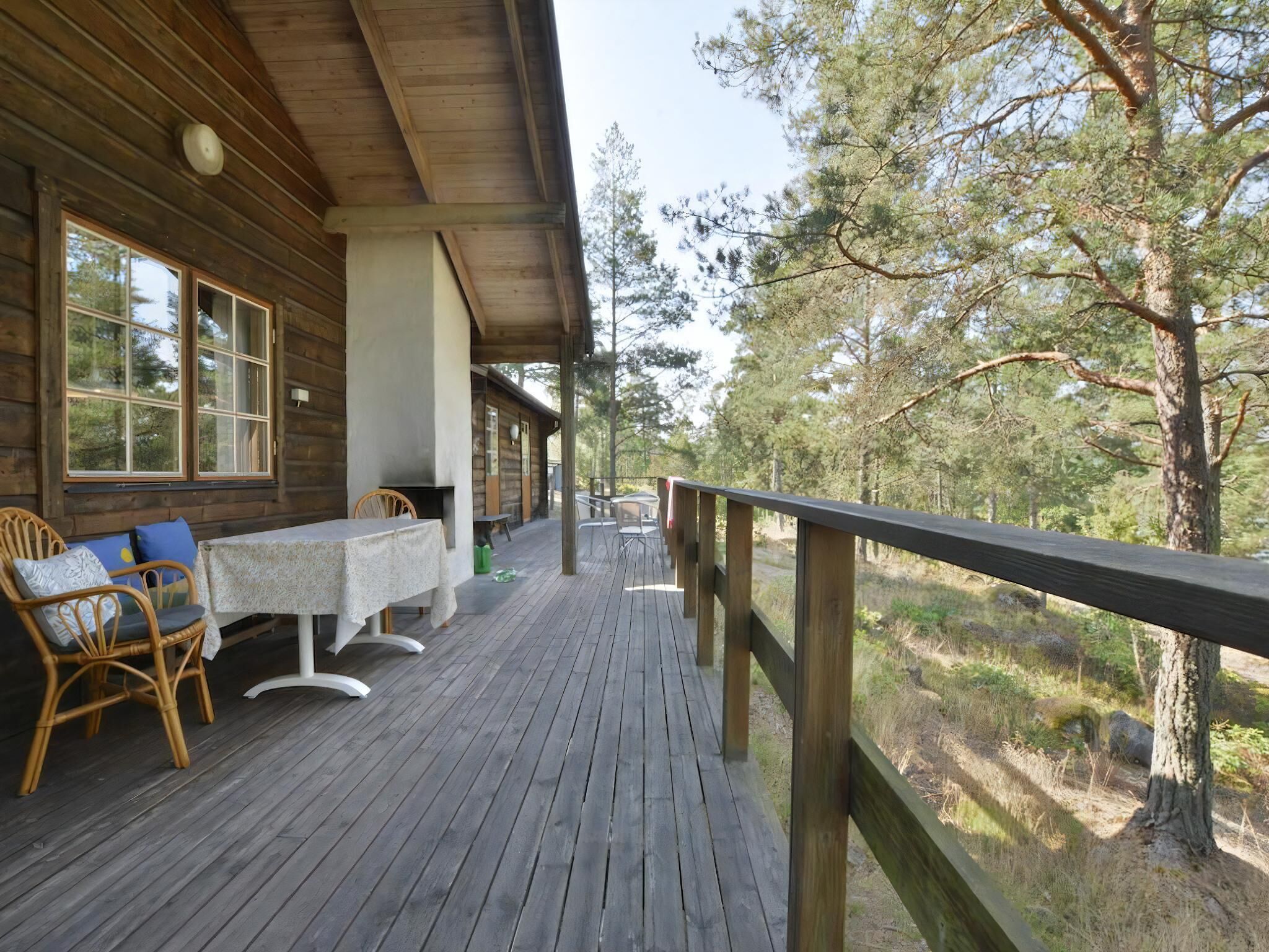 Une terrasse en bois avec une table et des chaises, donnant sur une zone boisée.