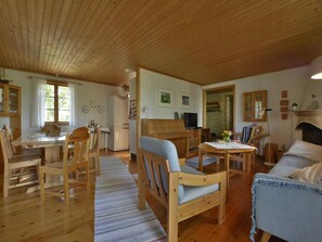 A wooden interior with a dining area, a sofa, a TV, and a fireplace. - Lovely log house with a view of the sea (Figeholm)