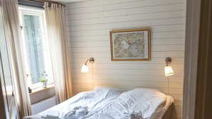 Um quarto com cama, janela com cortinas, mapa fixado na parede e luminária no teto.