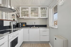 A modern kitchen with white cabinets, a Bosch oven, a sink, and a window with a view. - Holiday home for 6 near beach and Hals town (Hals)