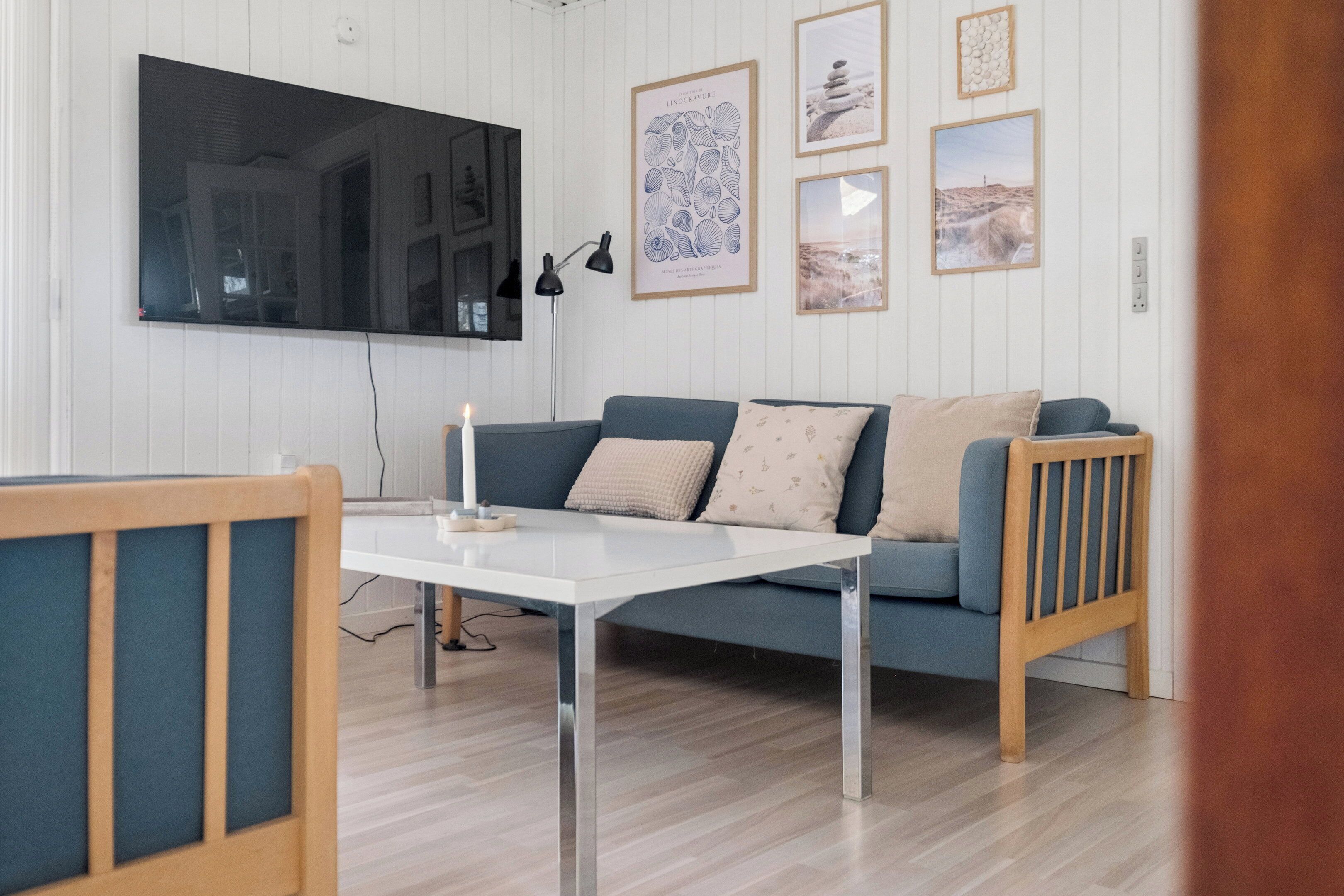 A living room with a TV, a sofa, a table, and framed pictures on the wall.
