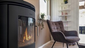 Ein modernes Wohnzimmer mit Kaminofen, einem gemütlichen Sessel und einer weißen Regaleinheit mit Dekoration.