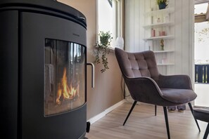 Un salon moderne avec un poêle à bois, un fauteuil confortable et une étagère blanche où sont disposés des objets décoratifs.