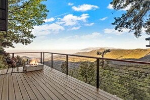 Una terraza de madera con un pozo de fuego y asientos, con vistas a un paisaje montañoso.