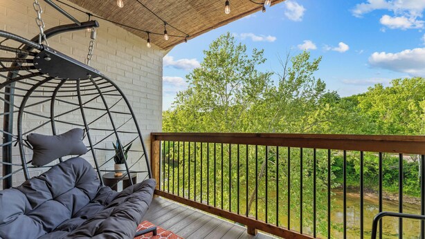 Un balcon avec un fauteuil suspendu, un lit et une vue sur une rivière et des arbres.