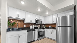 Une cuisine moderne avec des armoires blanches, des appareils en acier inoxydable et un mur d’accent en bois.