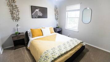 A bedroom with a bed, nightstand, lamp, and decorative wall art.