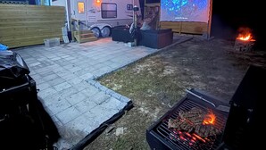 Un càmping amb una caravana, una pantalla de televisió portàtil i una barbacoa.