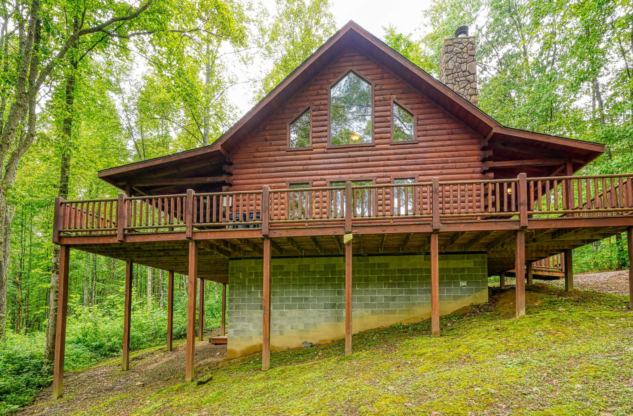 A wooden cabin with a balcony, surrounded by forest.