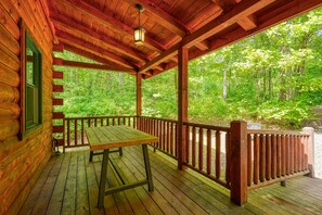 Una baita di legno con un portico coperto, un tavolo da picnic e vista su una foresta.