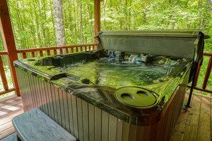 Ein Whirlpool mit Holzterrasse und Metallgeländer, umgeben von Bäumen.