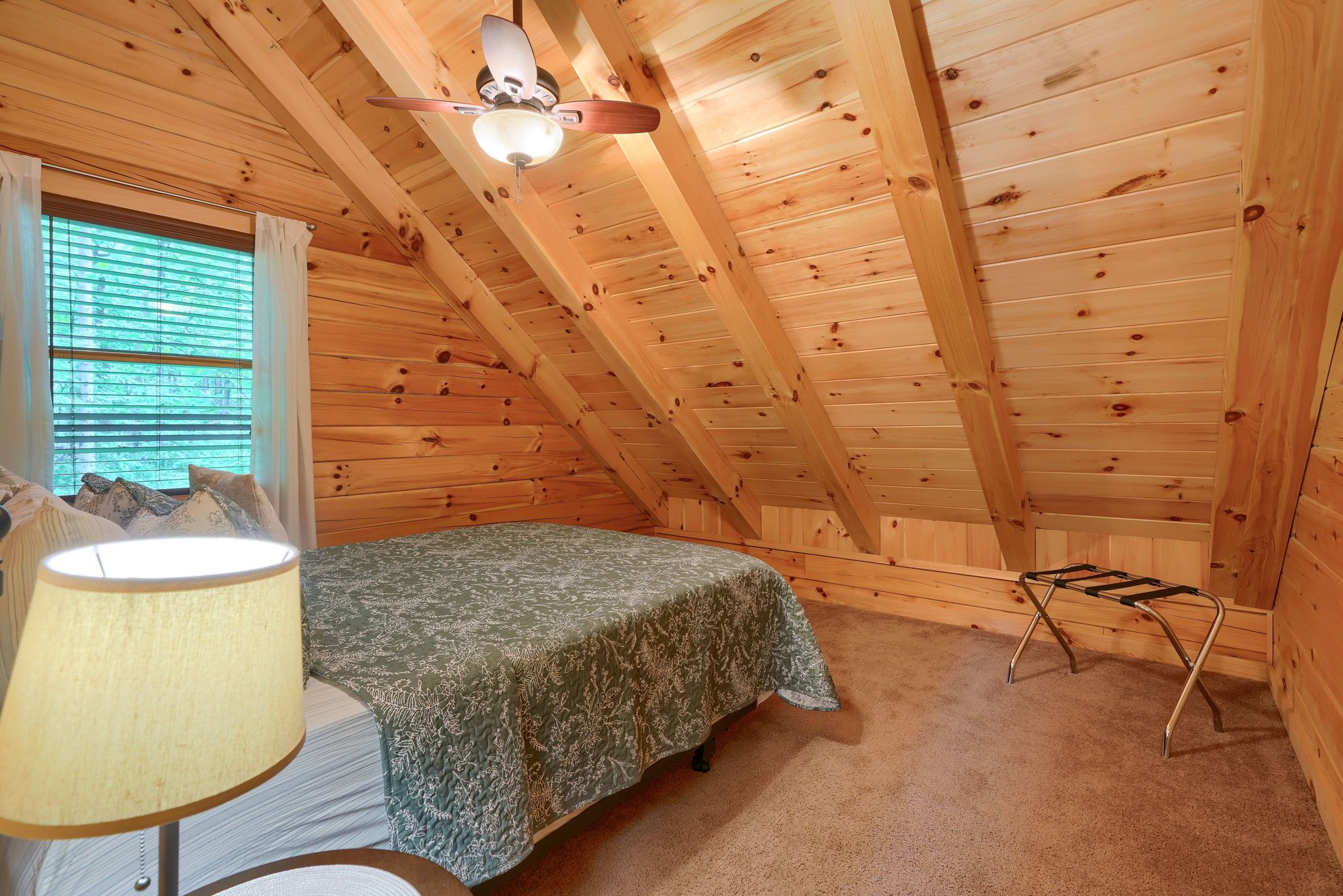A bedroom with a bed, a nightstand, a lamp, a window with blinds, and a ceiling fan.