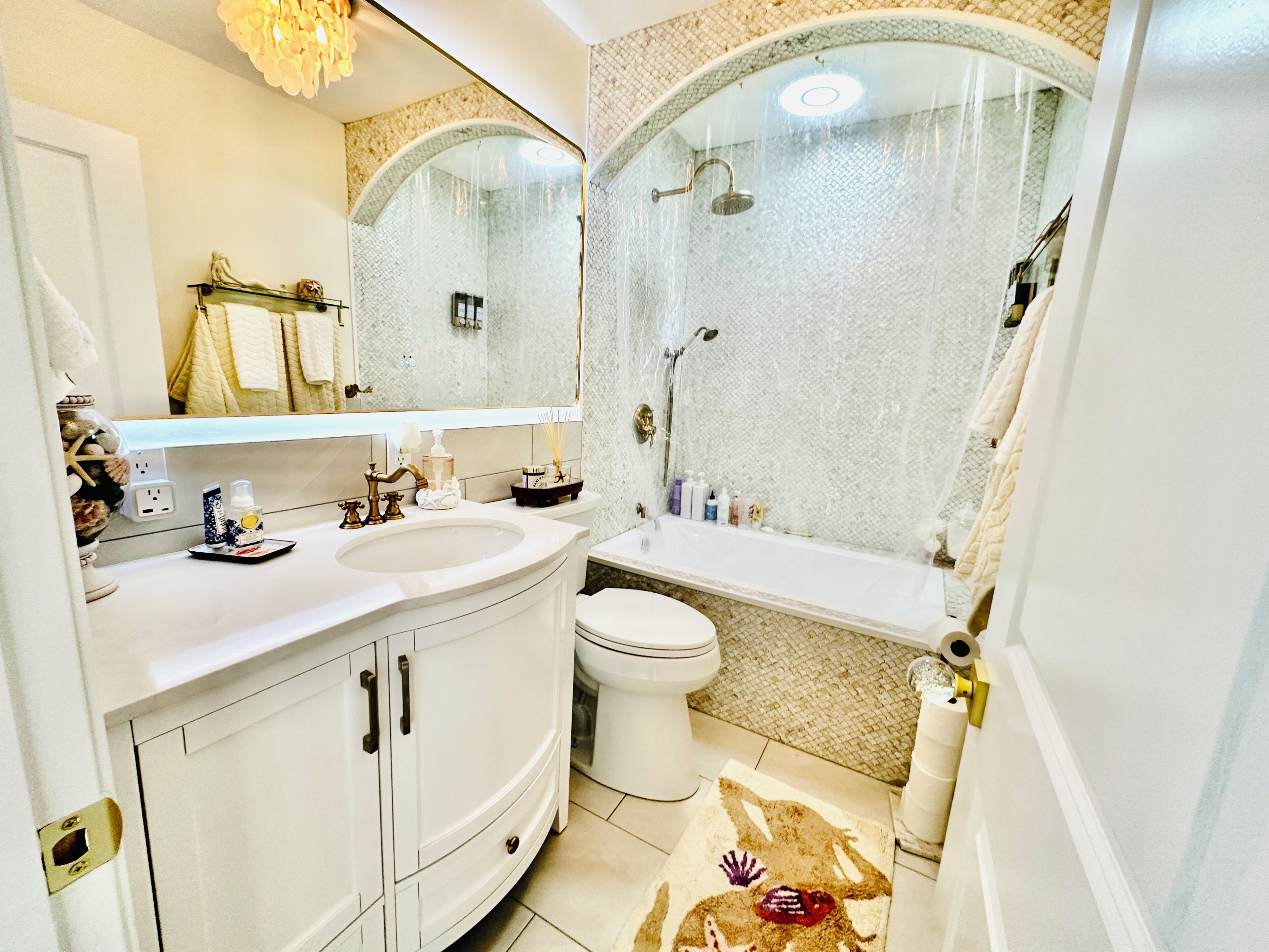 Een badkamer met een wit wastafelmeubel, een toilet en een douche met een glazen cabine. Boven de spiegel hangt een handdoekhouder.