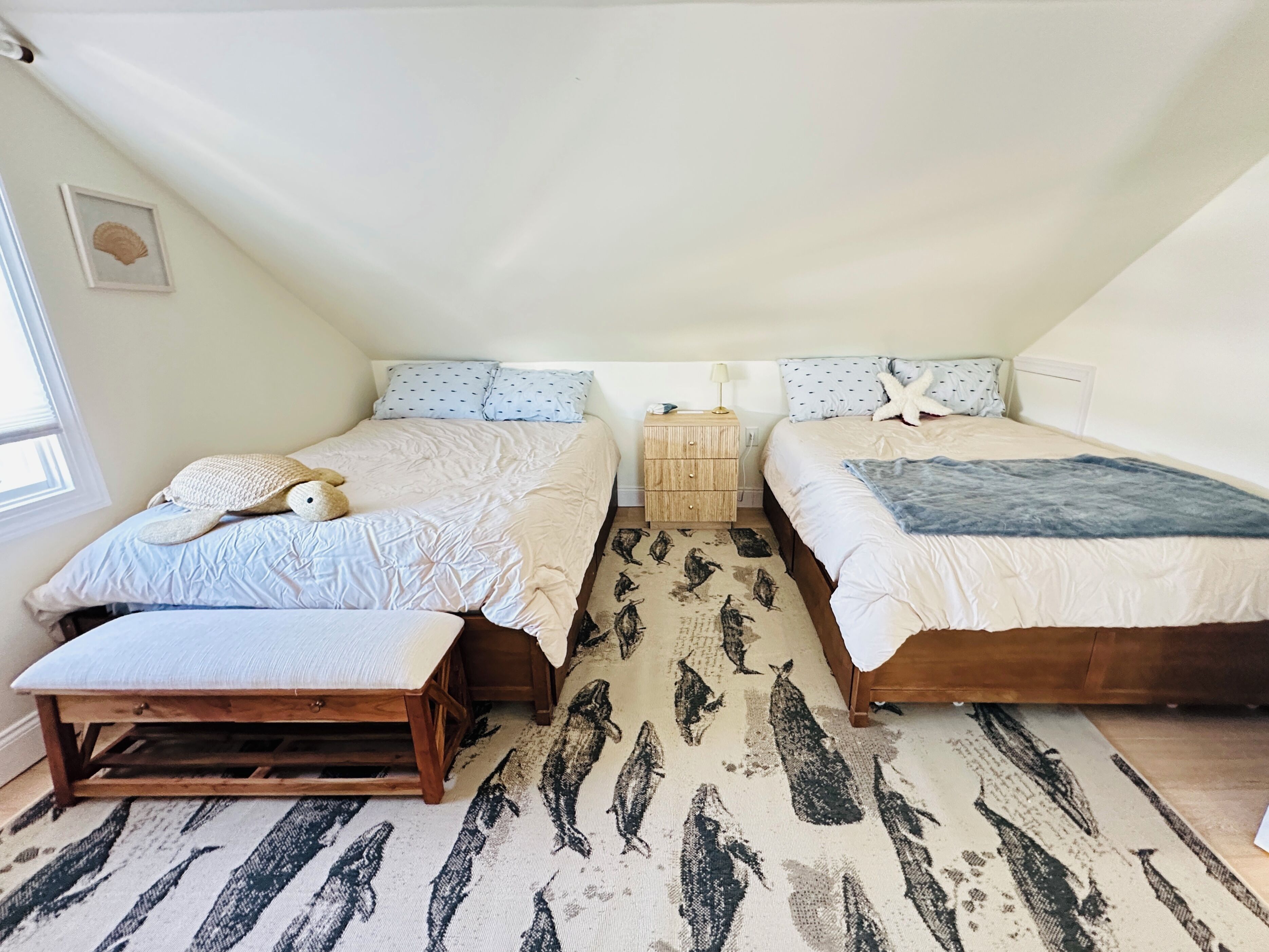 A bedroom with two beds, a wooden nightstand, a starfish pillow, and a patterned rug.