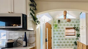 A kitchen with wooden cabinets, a built-in microwave, and a window with a view. - Sandy Buns Bungalow Beach House Escape (Ventnor City)
