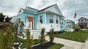 A two-story house with a front porch, a small garden, and a flag. - Sandy Buns Bungalow Beach House Escape (Ventnor City)
