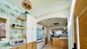 A kitchen with wooden cabinets, a white refrigerator, and a blue stove. - Sandy Buns Bungalow Beach House Escape (Ventnor City)