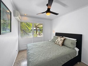 Una camera da letto con un letto, una ventola a soffitto, una finestra con persiane e un condizionatore d'aria.